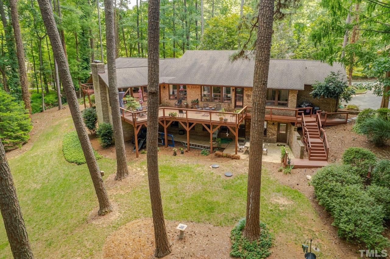 A view from above - a large home on a wooded lot with many trees, a large back deck, and covered patio